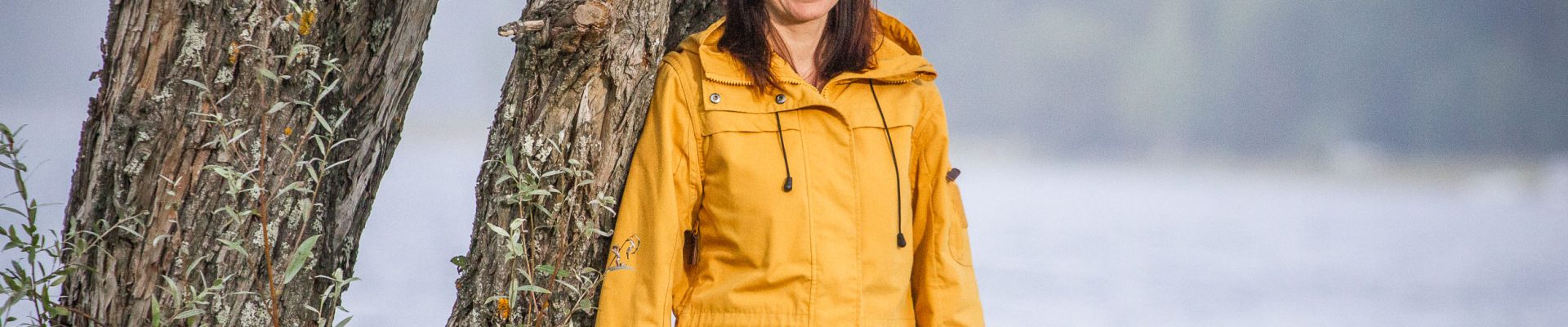 Henkilö keltaisessa takissa järven rannalla puun vieressä