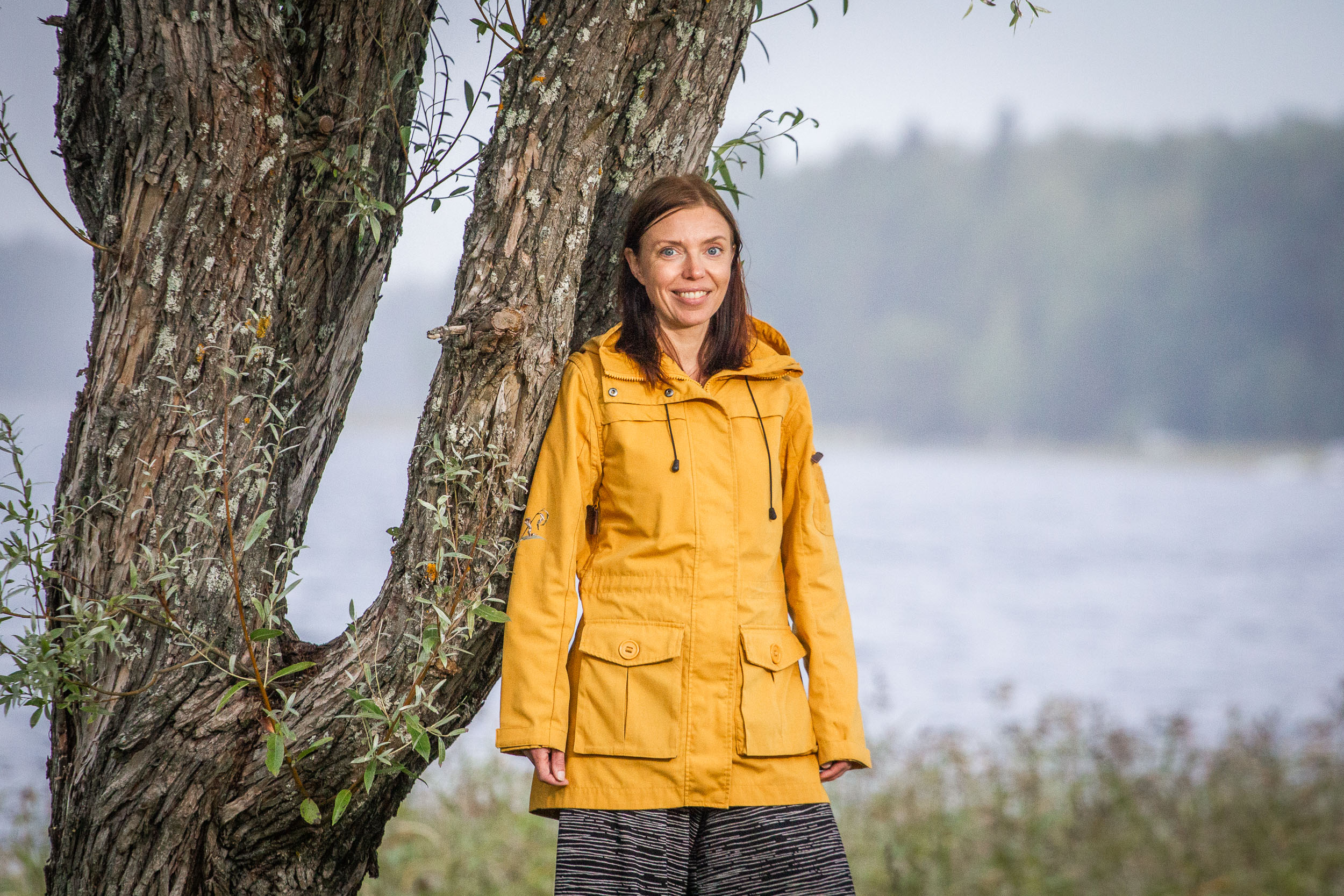 Henkilö keltaisessa takissa järven rannalla puun vieressä