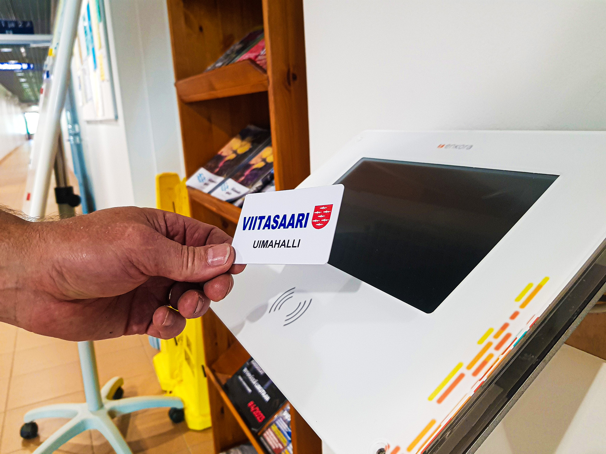 Henkilön käsi pitää Uimahalli Simmarin asiakaskorttia kortinlukulaitteen edustalla
