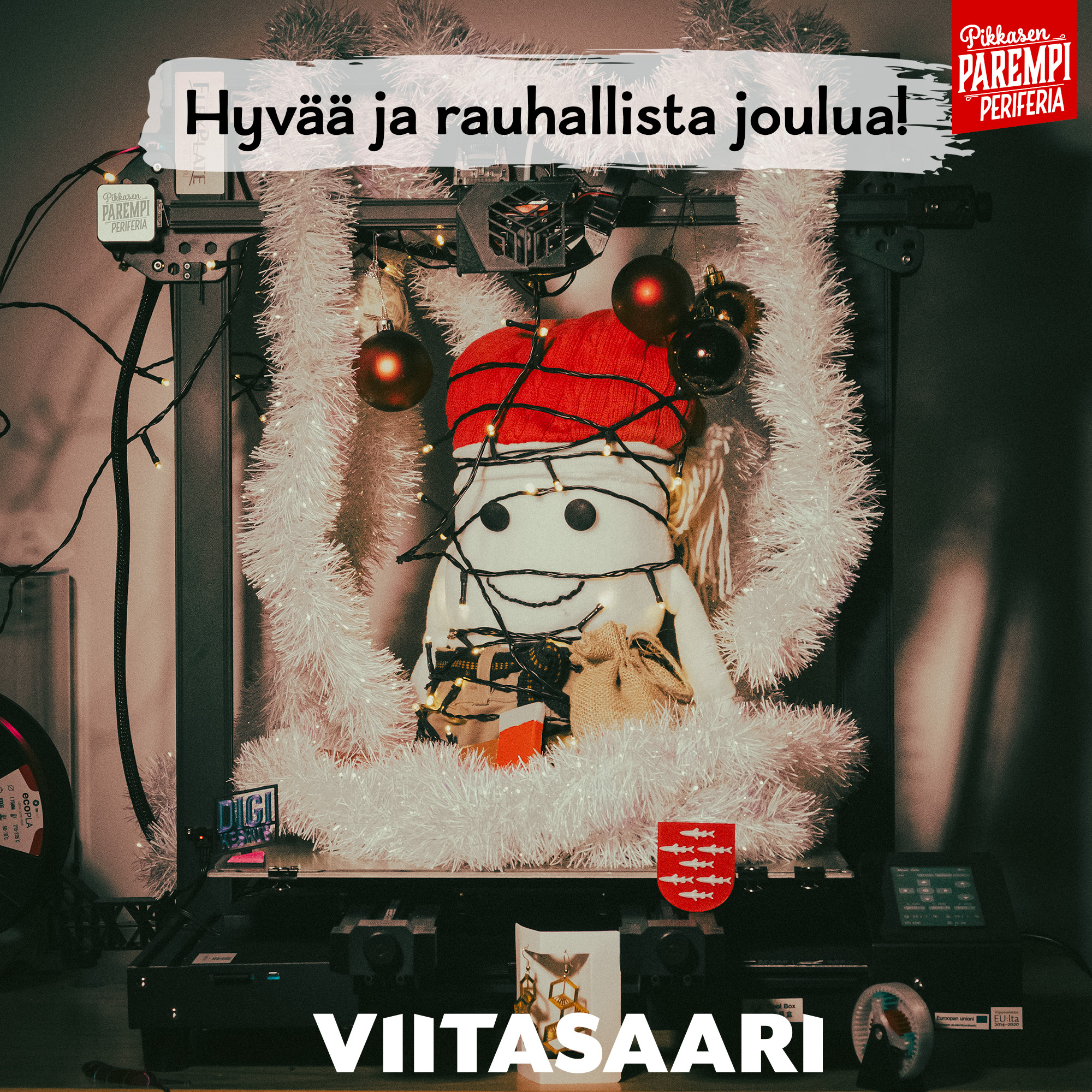 Pölkkypää-pehmohahmo 3d-tulostimessa, jossa led-valoja ja jouluköynnöstä, teksti Hyvää ja rauhallista joulua sekä Viitasaari-logo