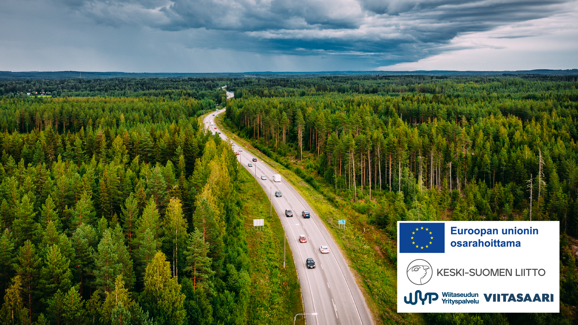 Ilmakuva, jossa metsää, tie autoineen ja taivasta. Myös EU, Keski-Suomen liitto, Wiitaseudun yrityspalvelu ja Viitasaaren kaupunki -logot.