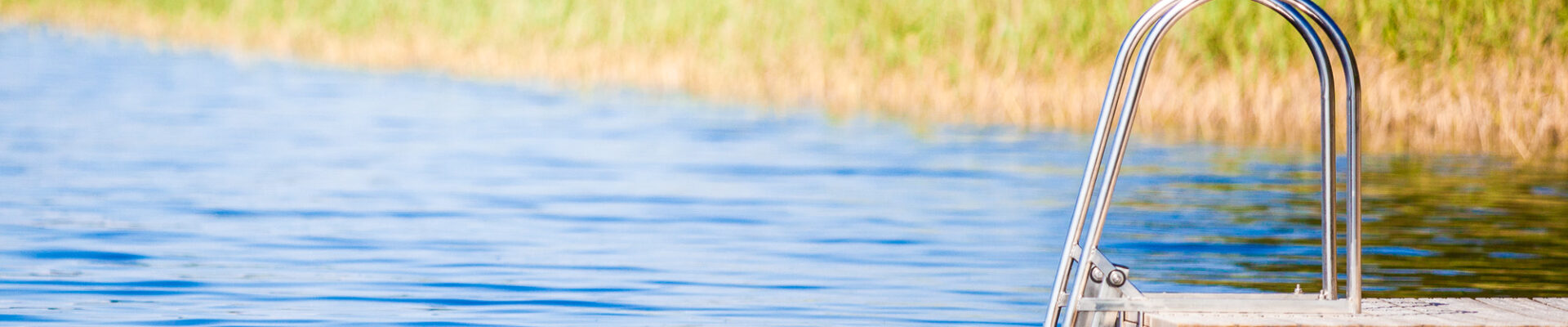 Kesäinen kuva laiturista Viitsaarella. Taustalla kaisloja, järvi on sininen.